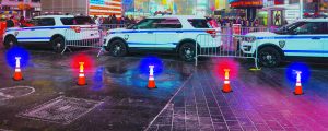 Line of police cars behind a row of cone flairs and metal barriers.