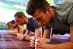 fitness, sport, exercising and people concept - close up of man doing plank exercise at group training in gym