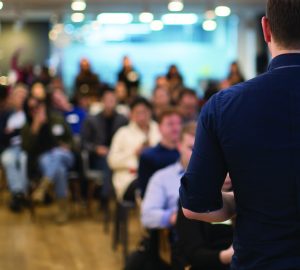 Speaker addressing group. Businessman entrepreneur giving a lecture to a sold-out crowd in a lecture hall. Speaker talking in seminar. Speaker at business conference or presentation stock photo. Male CEO talking during a business presentation in a board room. Copy space. Business coach concept.