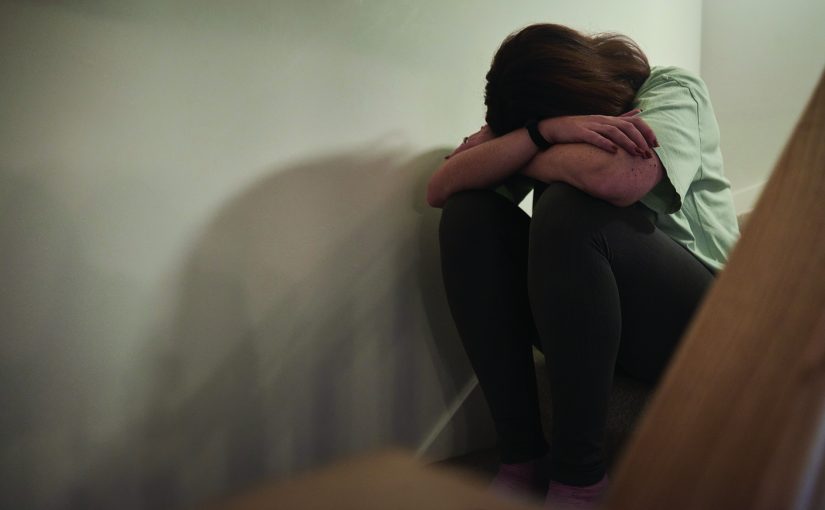 A woman suffering from depression or domestic abuse sat on the stairs of her home hiding her face.