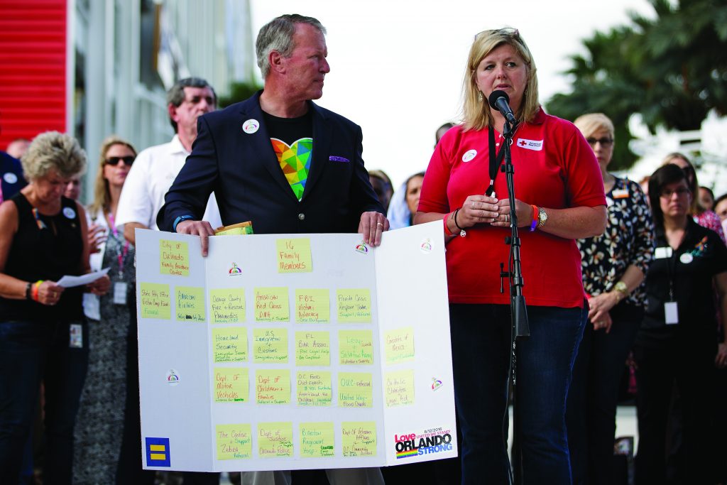 ORLANDO, FL - JUNE 17: Surrounded by members of federal, state and local agencies, Orlando Mayor Buddy Dyer (L) looks on as Red Cross volunteer Amy Decker (R) speaks at a press conference to provide an update on the assistance being provided to victims' families at the Orland Family Assistance Center, at Camping World Stadium, June 17, 2016 in Orlando, Florida. The shooting at Pulse Nightclub, which killed 49 people and injured 53, is the worst mass-shooting event in American history. (