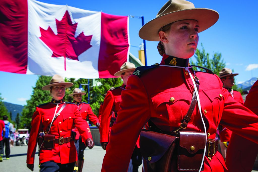 Officers of the Royal Canadian Mounted Police, dressed in traditional red serge uniforms, marching during Canada Day in Whistler, British Columbia