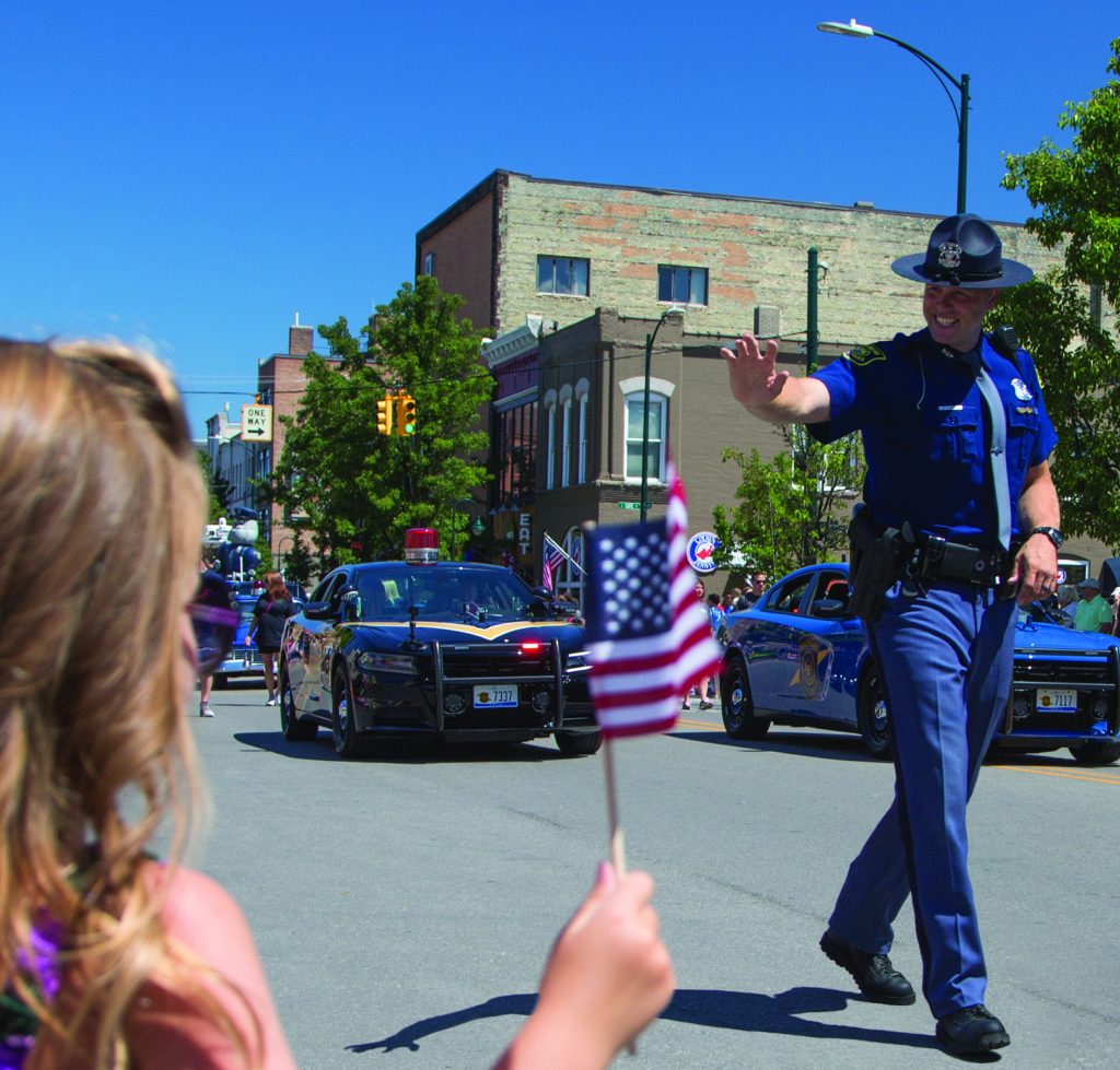 State Trooper waves at bystander as he walks in the Traverse City National Cherry Festival Parade