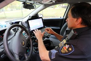 Images shows sergeant in patrol vehicle using tablet with keyboard.